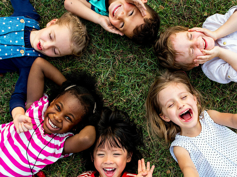 Mehrere Kinder unterschiedlicher Hautfarbe liegen im Kreis im Gras.