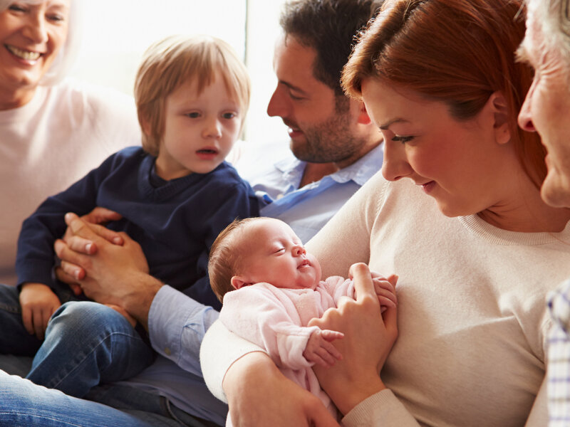 Neugeborenes Kind mit Eltern, Großeltern und Geschwisterkind im Wohnzimmer